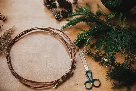 Making christmas wreath.Fir branches, pine cones, thread, scissors, wooden circle, berries and herbs for rustic wreath on wooden table. Details for workshop of making christmas wreathの写真素材