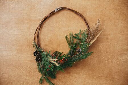 Creative rustic christmas wreath on wooden table, flat lay. Christmas wreath with fir branches, berries, pine cones and herbs on rural background. Copy space. Seasons greetingsの写真素材