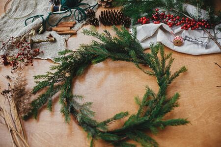 Fir branches, pine cones, thread, berries, cinnamon on wooden table. Rustic Christmas wreath workshop. Authentic stylish still life. Making Christmas wreath.の写真素材