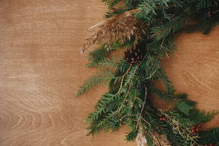 Creative rustic christmas wreath close up on wooden table. Details of christmas wreath with fir branches, berries, pine cones and herbs on rural background. Copy space. Seasons greetingsの写真素材