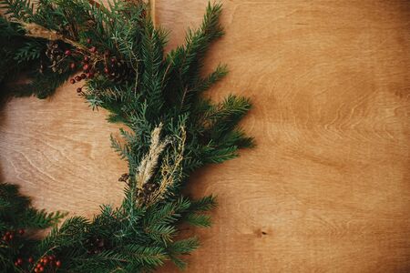 Christmas rustic wreath flat lay. Creative rural christmas wreath with fir branches, berries, pine cones and herbs on wooden table. Copy space. Seasons greetingsの写真素材