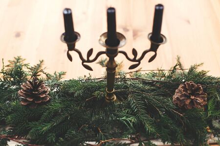 Stylish rustic christmas arrangement for festive dinner. Fir green branches with pine cones and vintage candlestick with black candles on wooden table. Christmas rural decor, table settingの写真素材