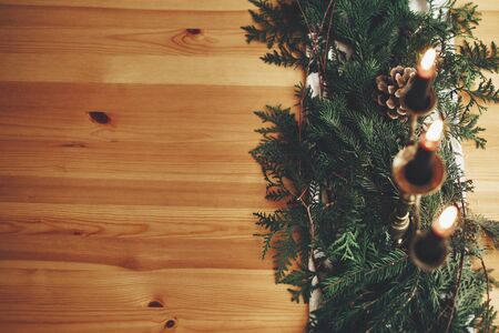 Fir branches with pine cones and vintage candlestick with burning black candles on wooden table. Stylish rustic christmas arrangement for festive dinner. Christmas rural table decor for feastの写真素材