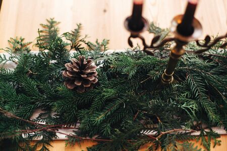 Fir branches with pine cones and vintage candlestick with burning black candles on wooden table. Stylish rustic christmas arrangement for festive dinner. Christmas rural table decor for feastの写真素材