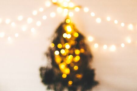 Abstract christmas tree. Blurred image of christmas tree made of pine branches with golden festive lights hanging on white wall. Alternative christmas tree. Scandinavian minimal decorの写真素材