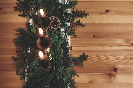 Fir branches with pine cones and vintage candlestick with black candles on wooden table. Copy space. Stylish rustic christmas arrangement for festive dinner. Christmas rural table decorの写真素材