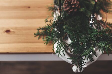 Stylish rustic christmas arrangement for festive dinner closeup. Fir branches with pine cones and vintage candlestick with black candles on linen cloth on wooden table. Christmas rural decorの写真素材