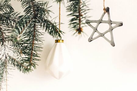 Stylish christmas ornaments on fir branch hanging on white wall. Creative christmas festive decor. Pine branch with vintage glass toys. Modern Scandinavian minimal decorationの写真素材