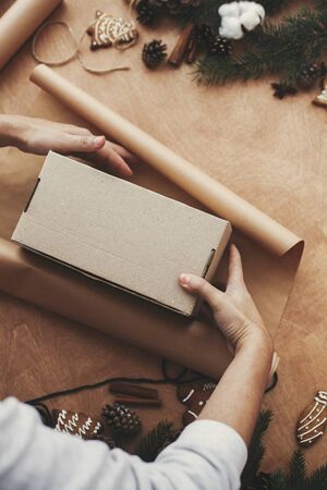 Hands wrapping christmas gift in craft paper and pine branchesの写真素材