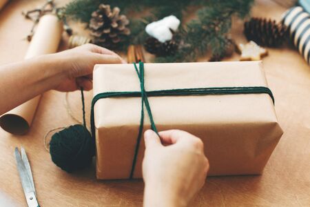 Hands wrapping christmas gift in stylish striped paper and pine branches