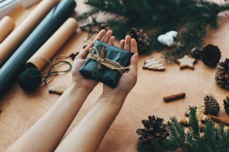 Hands wrapping christmas gift in stylish striped paper and pine branchesの写真素材