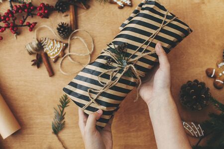 Hands wrapping christmas gift in stylish striped paper and pine branches
