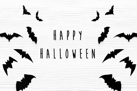 Happy Halloween text, greeting card flat lay. Black bats on white wooden background. Modern minimal halloween paper diy decorations. Halloween signの写真素材