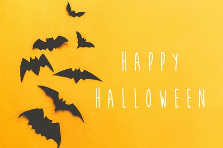 Happy Halloween text, greeting card. Black bats flying on bright yellow paper background. Flat lay. Modern spooky minimal halloween decor. Halloween signの写真素材