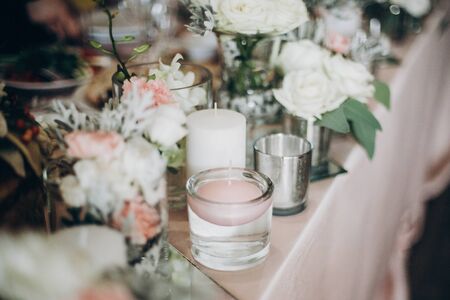 Candle, White  flowers in modern glass vase on pink centerpiece. Stylish luxury decor on wedding...