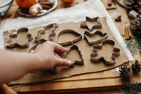 Making christmas gingerbread cookies. Hand cutting raw dough with  metal cutters and anise, ginger, cinnamon, pine cones, fir branches on rustic table.の写真素材