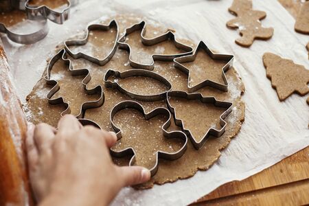 Making christmas gingerbread cookies. Hand cutting raw dough with  metal cutters and anise, ginger,...