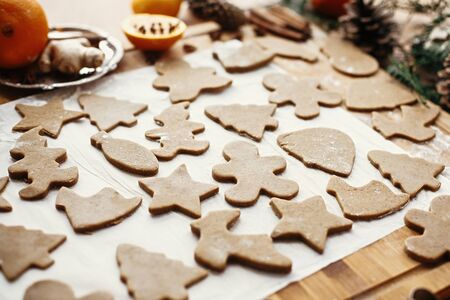 Making christmas gingerbread cookies. Raw dough in shape of gingerbread man,christmas tree, star, deer on paper and  anise, cinnamon, pine cones on rustic table.の写真素材