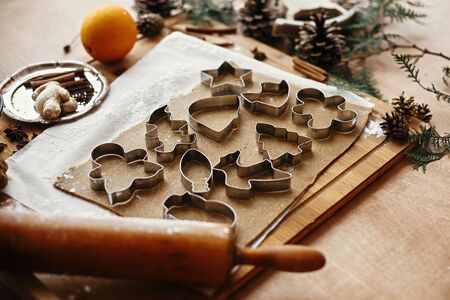 Gingerbread dough with metal cutters in different shapes for christmas cookies and wooden rolling pin, anise, ginger, cinnamon, pine cones, fir branches, flour on rustic tableの写真素材