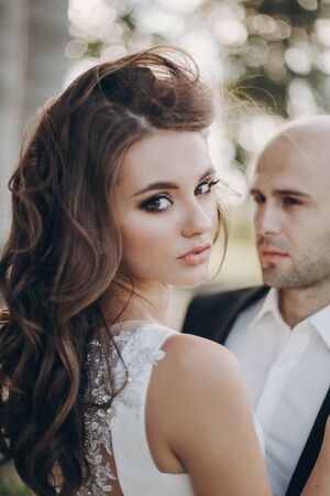 Gorgeous bride and groom embracing in evening sunlight near old castle in park. Romantic moment. Stylish wedding couple gently hugging and smilingの写真素材