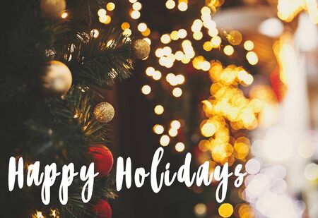 Happy Holidays  text sign on stylish christmas fir branches with golden lights , red festive baubles and bow on  window store at holiday market in city street. Seasons greeting cardの写真素材