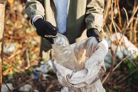 Eco activist  picking up dirty plastic bottles in park. Woman hand in glove picking up trash,...