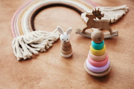 Eco friendly plastic free toys for toddler. Stylish wooden toys for child on wooden table. Modern colorful wooden pyramid with rings, wooden bunny and macrame rainbow.の写真素材