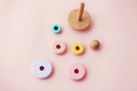 Stylish wooden toys for child on pink background, flat lay. Modern colorful wooden pyramid with disassembled rings. Eco friendly, plastic free toys for toddlerの写真素材