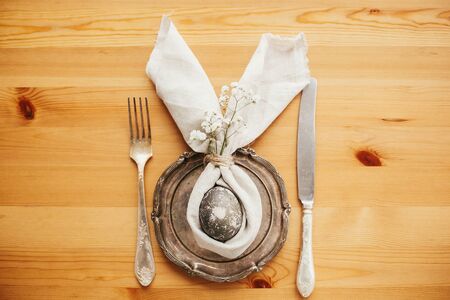 Stylish Easter brunch table setting with egg in easter bunny napkin. Modern natural dyed gray egg on...