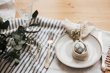 Stylish Easter brunch table setting with egg in easter bunny napkin. Modern natural dyed blue egg on napkin with bunny ears, flowers on plate and vintage cutlery. Easter table decorationsの写真素材