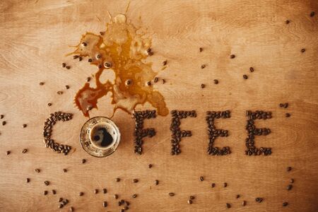 Coffee word made of  roasted coffee beans and spilled coffee from glass cup of hot espresso on wooden table, flat lay with copy space. International coffee day. Creative ideaの写真素材