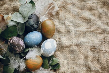 Stylish easter eggs in rustic nest with feathers on rustic table. Natural dyed easter eggs with...