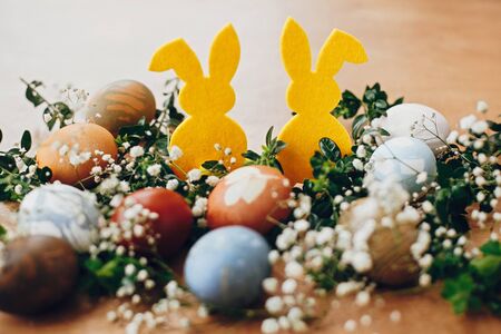 Happy Easter. Stylish easter eggs, yellow bunny in nest of spring flowers on rustic wooden table,...