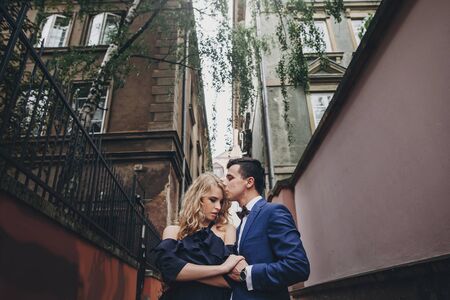 Stylish couple embracing and kissing in european city street. Sensual passionate moment. Fashionable man and woman in love gently hugging. Valentines dayの写真素材