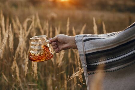 Hand spilling out fresh hot coffee from glass flask in sunny warm light in rural herbs. Coffee splash and drops. Atmospheric tranquil moment. Alternative coffee brewing in travelの写真素材