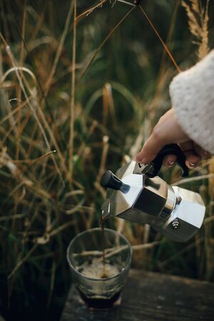 Hipster pouring fresh hot coffee from geyser coffee maker into glass cup in sunny warm light in rural countryside herbs. Atmospheric tranquil moment. Alternative coffee brewing in travelの写真素材