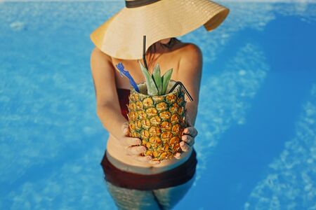 Beautiful young woman holding cocktail in pineapple and relaxing in pool, summer vacation. Girl in...