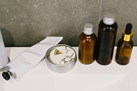Ubtan for skin in glass bottle, solid shampoo in metal can, tonic,  conditioner on white sink in...