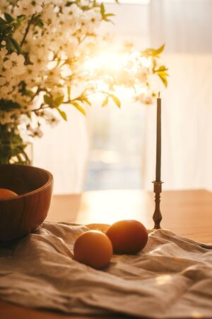 Natural Easter eggs and vintage candle in sunset warm light on linen fabric on rustic table with...