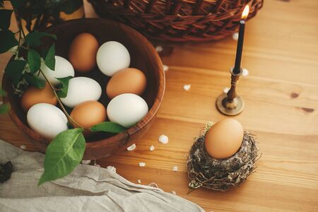 Natural Easter egg in rustic nest on background of candle, wicker basket, organic eggs, cherry flowers on wooden table. Happy Easter, atmospheric moment. Rural still life.  Zero wasteの写真素材