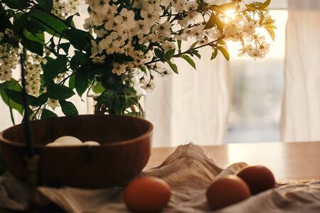Happy Easter, atmospheric moment. Natural Easter eggs in sunset warm light on linen rustic fabric with cherry flowers and green leaves. Rural still life. Organic white and brown eggsの写真素材