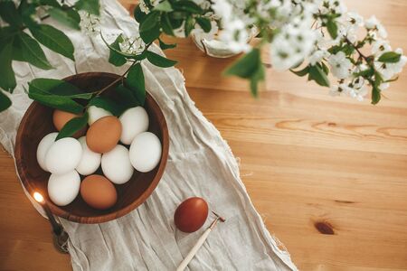 Rural Easter flat lay. Natural eggs in wooden bowl and vintage candle on linen fabric on background...
