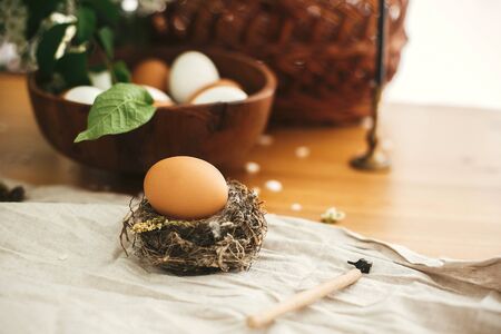 Zero waste Easter holidays. Natural Easter egg in rustic nest on background of candle, wicker...
