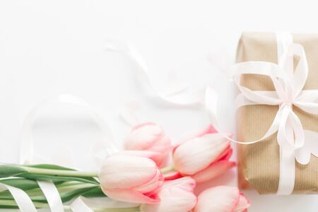 Pink tulips with ribbon and gift box on white background. Space for text. Stylish soft image of spring flowers. Greeting card mockupの写真素材