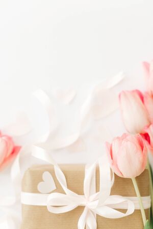 Pink tulips with ribbon and gift box on white background, flat lay. Stylish vertical image. Happy womens day. Greeting card with space for text. Wedding or valentine mockupの写真素材