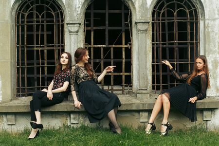 three gorgeous women in black sitting at old church in the city and posing, stylish gothic themed, ladies partyの写真素材