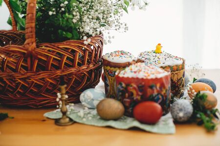 Easter cake, easter eggs natural dyed, candle, green branches and flowers on rustic wooden table with wicker basket. Traditional Easter Food for sanctify in churchの写真素材