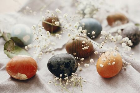 Happy Easter. Stylish easter eggs on rustic table. Natural dyed colorful easter eggs with spring white flowers and feathers on rural textile background.の写真素材