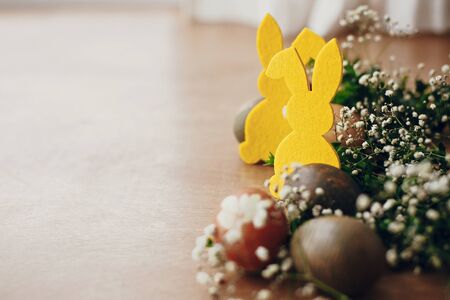 Happy Easter. Stylish easter eggs, yellow bunny in nest of spring flowers on rustic wooden table, space for text. Natural dyed easter eggs and rabbit decorations on wooden backgroundの写真素材