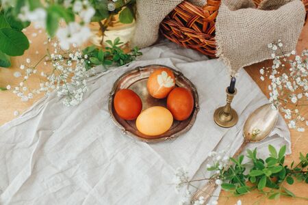 Modern Easter eggs on vintage plate on rustic table with spring flowers,candle, basket. Stylish red...